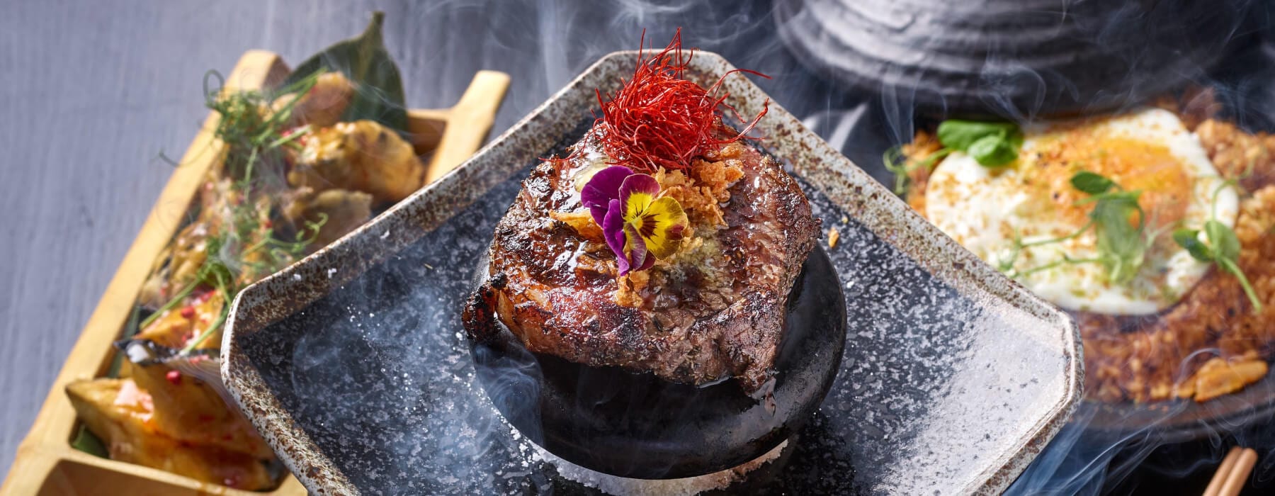 Wagyu smoking on a hot stone at the robata, chilli threads curling in the heat